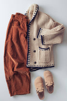 Knitted beige cardigan, brown pants, and tan shoes on a light gray background