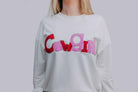 White sweatshirt with colorful letters spelling 'Cowgirl' on a plain background