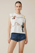 Woman wearing a white sleeveless top with embroidered  boot, rope and cactus designs on a beige background
