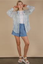 Front view of an oversized sky-blue brushstroke pleated button-down on model, showing drop shoulder, button cuff, and flowing crinkle texture.
