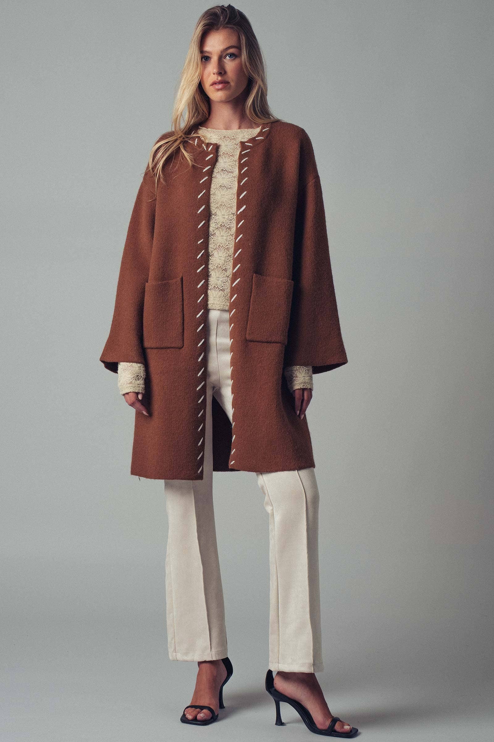 Woman wearing a brown open coat with white bold stitching  trim 