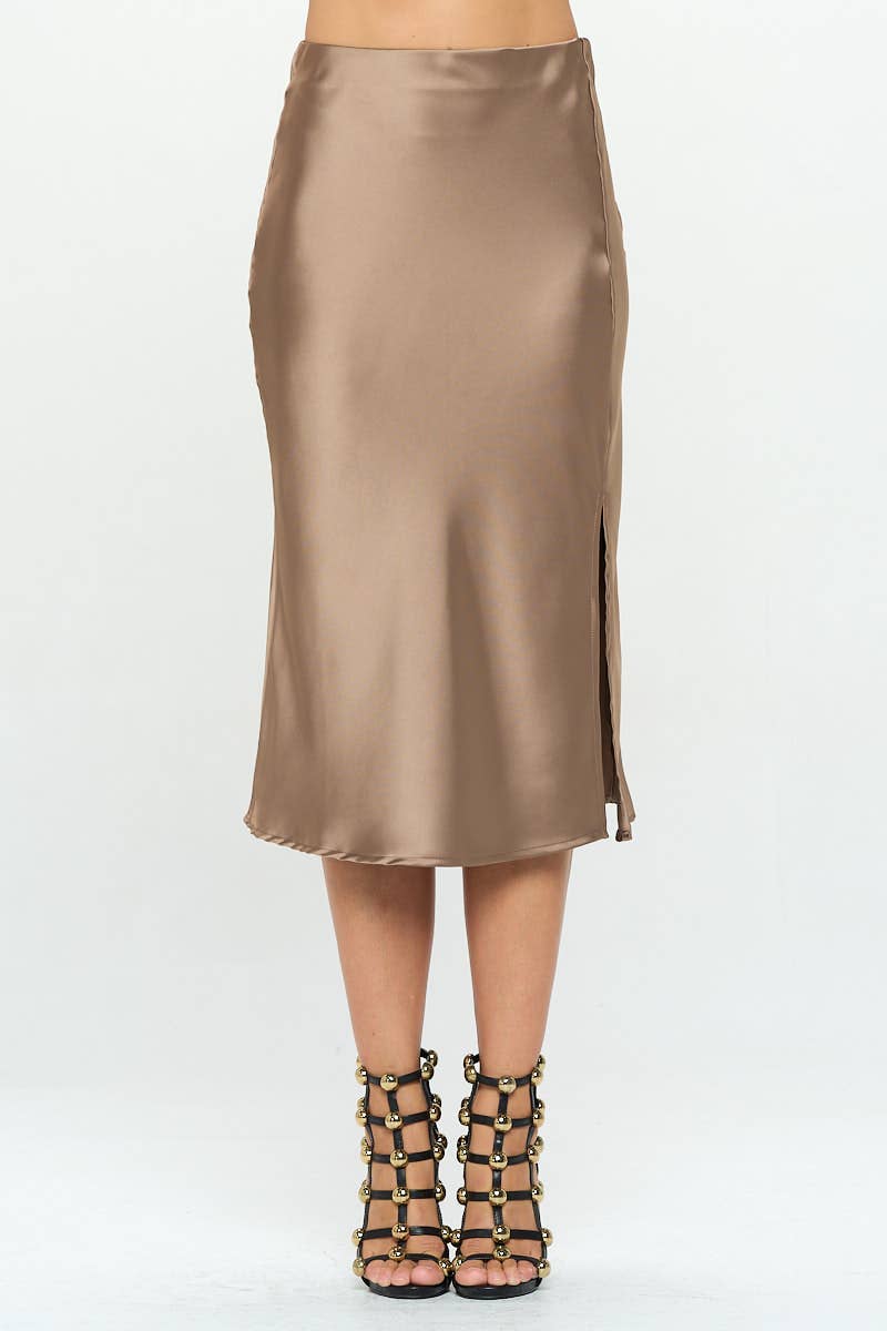 A woman modeling a satin midi skirt with a side slit, in a metallic color, paired with a satin top with a bow detail.