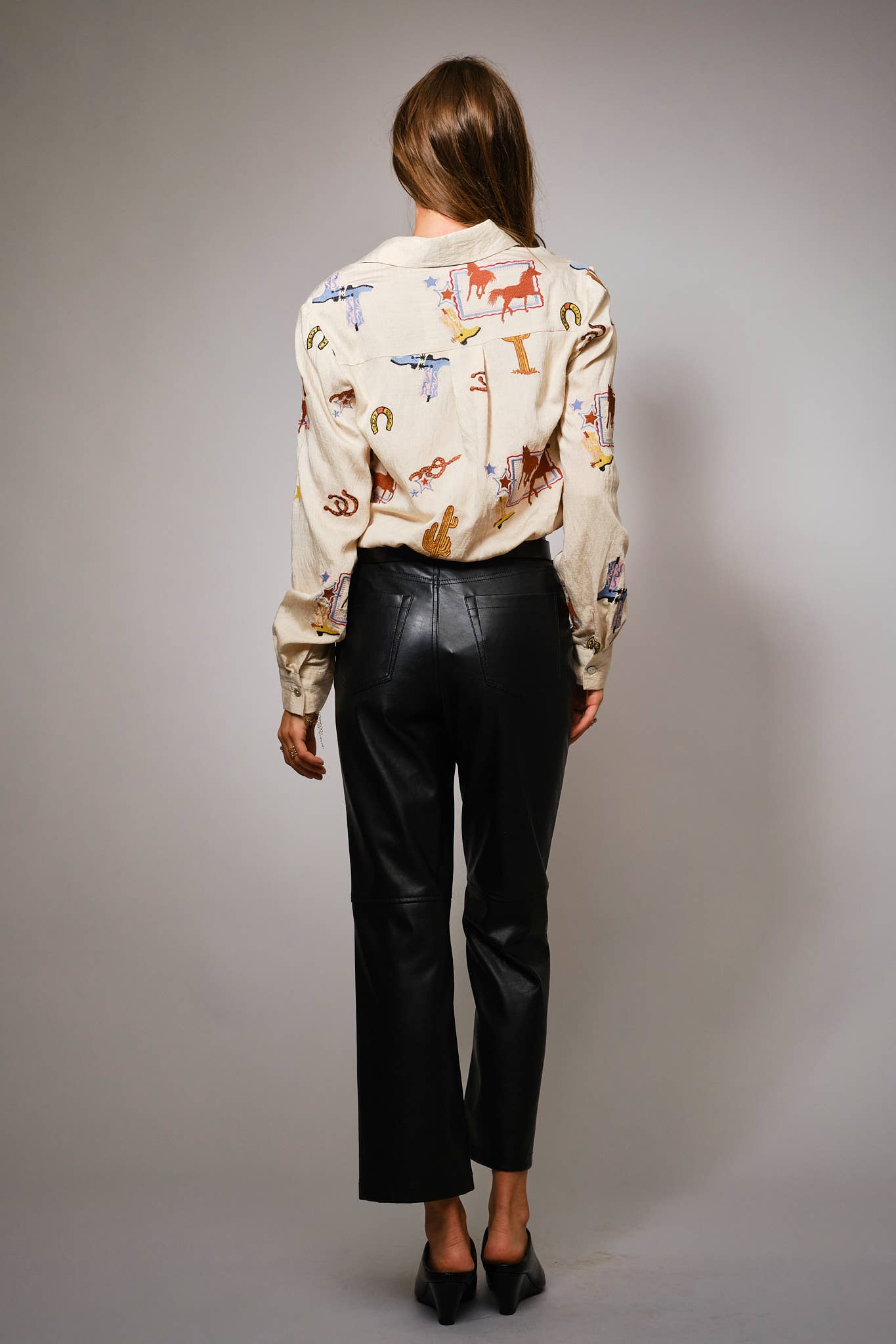 Person wearing a patterned shirt and black pants against a gray background
