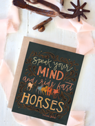 Card with 'Speak your mind and ride fast horses' text and horse illustrations on a wooden surface.