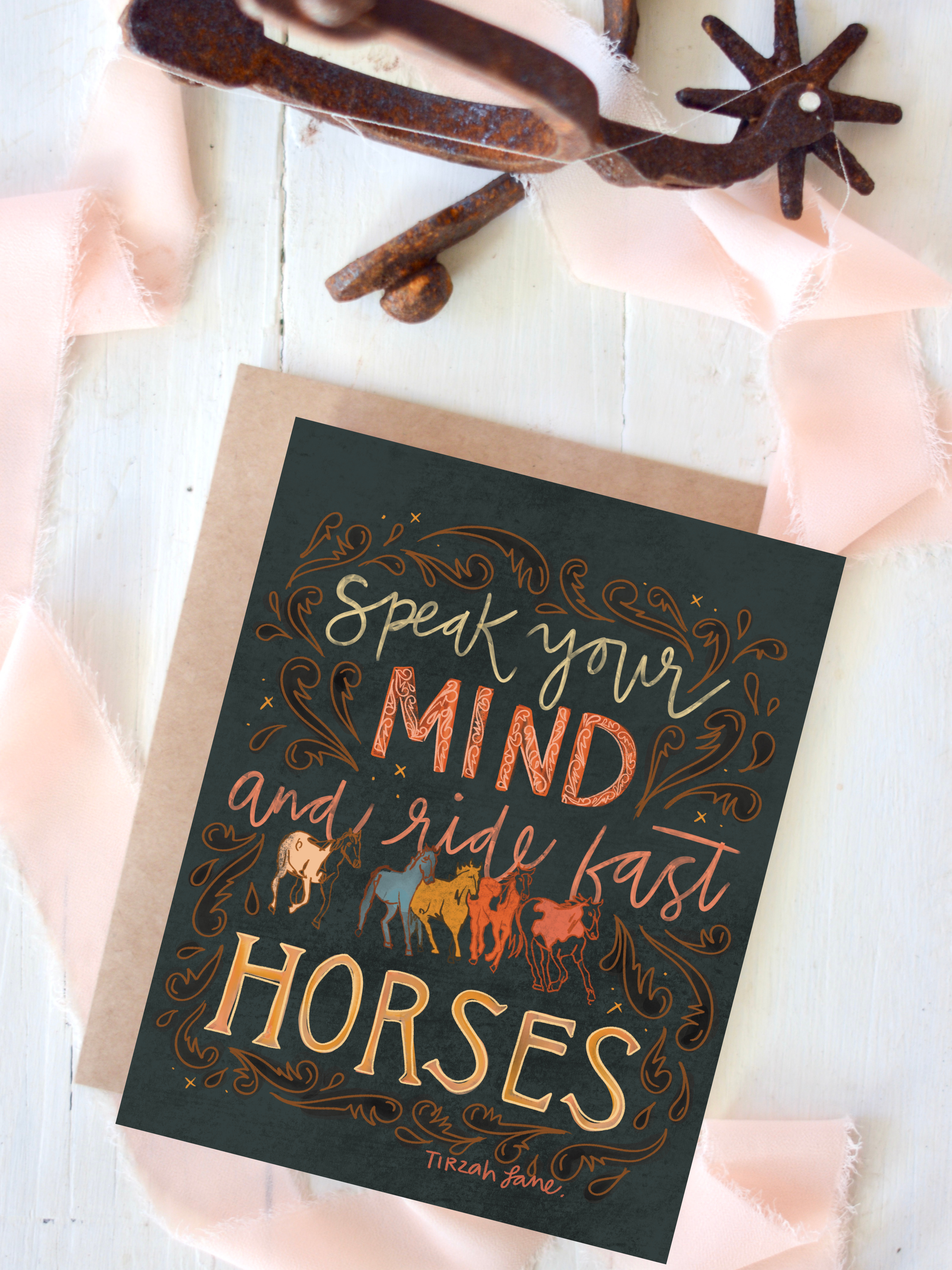 Card with 'Speak your mind and ride fast horses' text and horse illustrations on a wooden surface.
