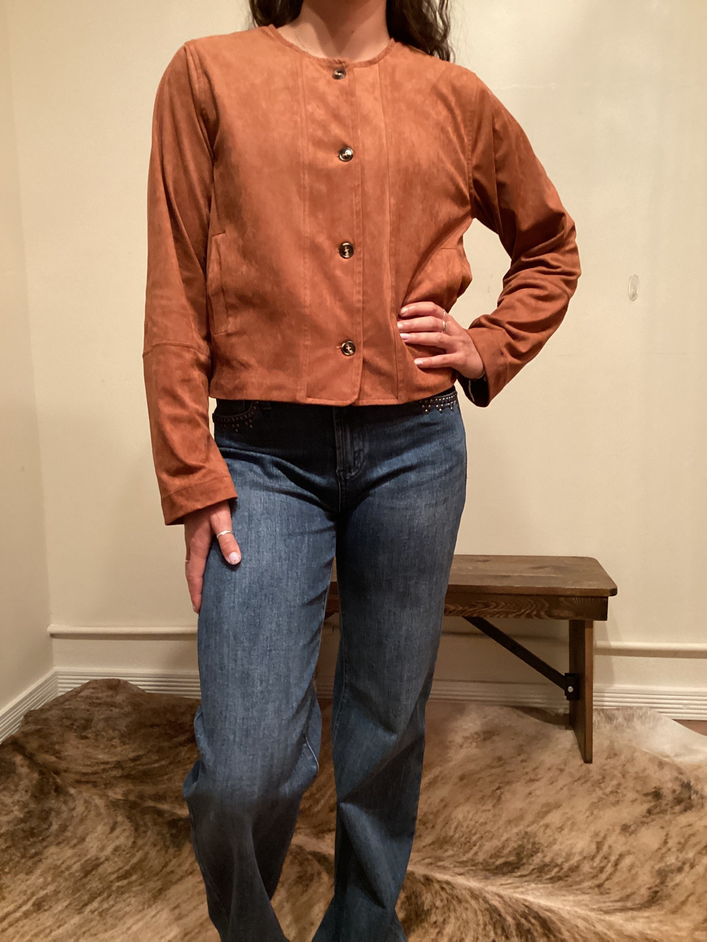 Person wearing a brown faux leather button up jacket and blue jeans 
