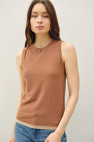 Woman wearing a brown sleeveless top and blue jeans against a plain background