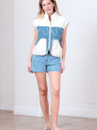 Model wearing indigo denim vest with white horseshoe print and faux-fur collar, zipped front, hands in pockets.”