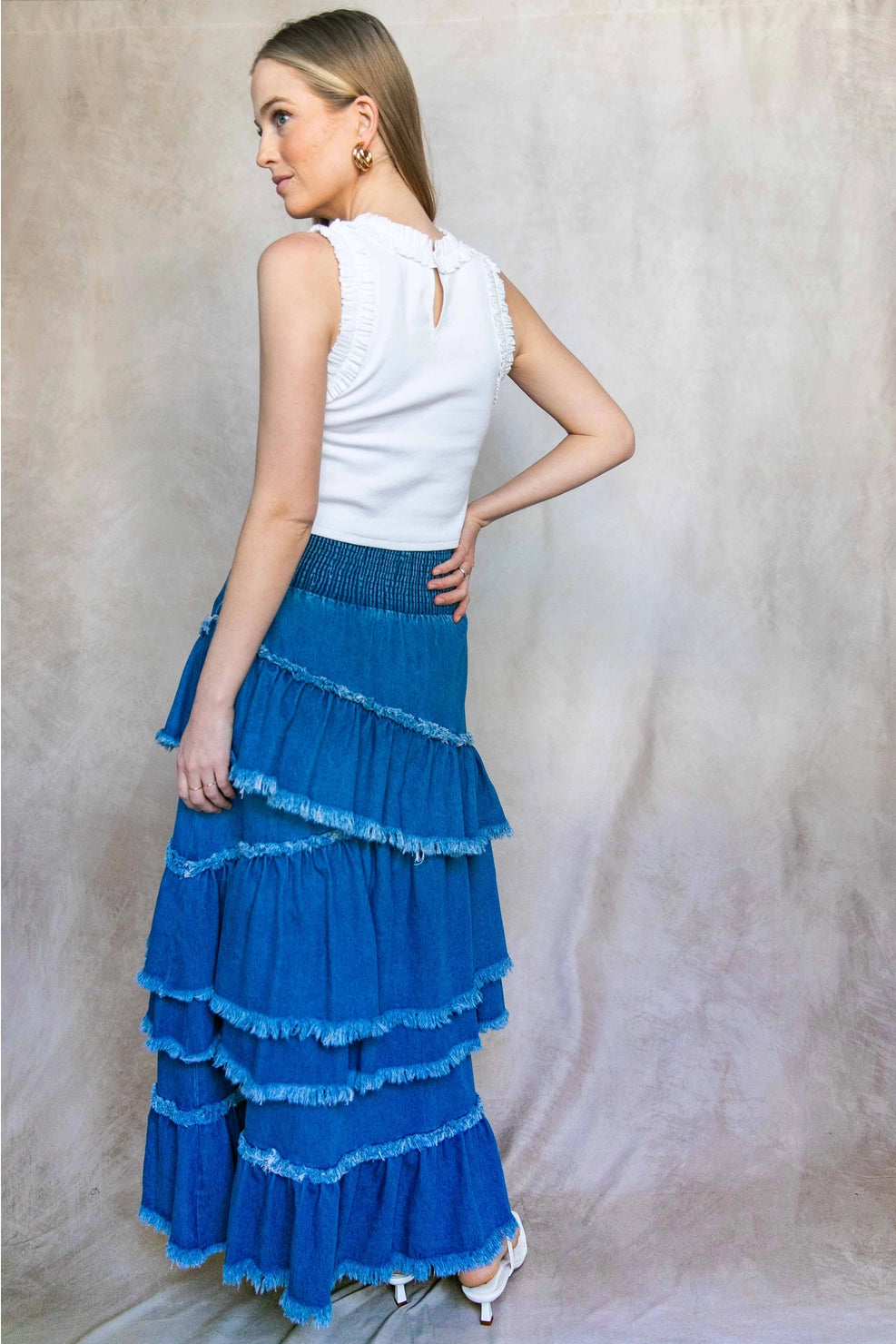 Woman wearing a white top and blue tiered skirt against a neutral background