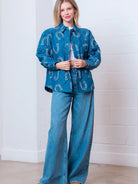 Front view of denim-blue quilted jacket with white horseshoe print and button front on model.