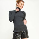 Woman wearing a dark gray turtleneck sweater and black leather shorts on a white background