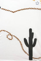 Woman wearing a white sleeveless top with embroidered  boot, rope and cactus designs on a beige background