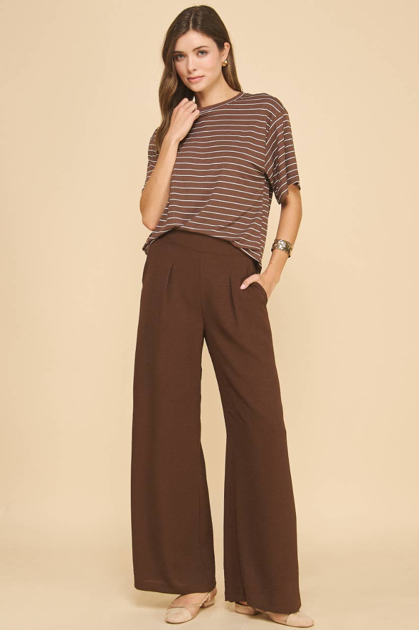 Woman wearing a striped shirt and brown wide-leg pants on a beige background