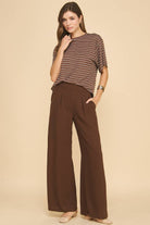 Woman wearing a striped shirt and brown wide-leg pants on a beige background