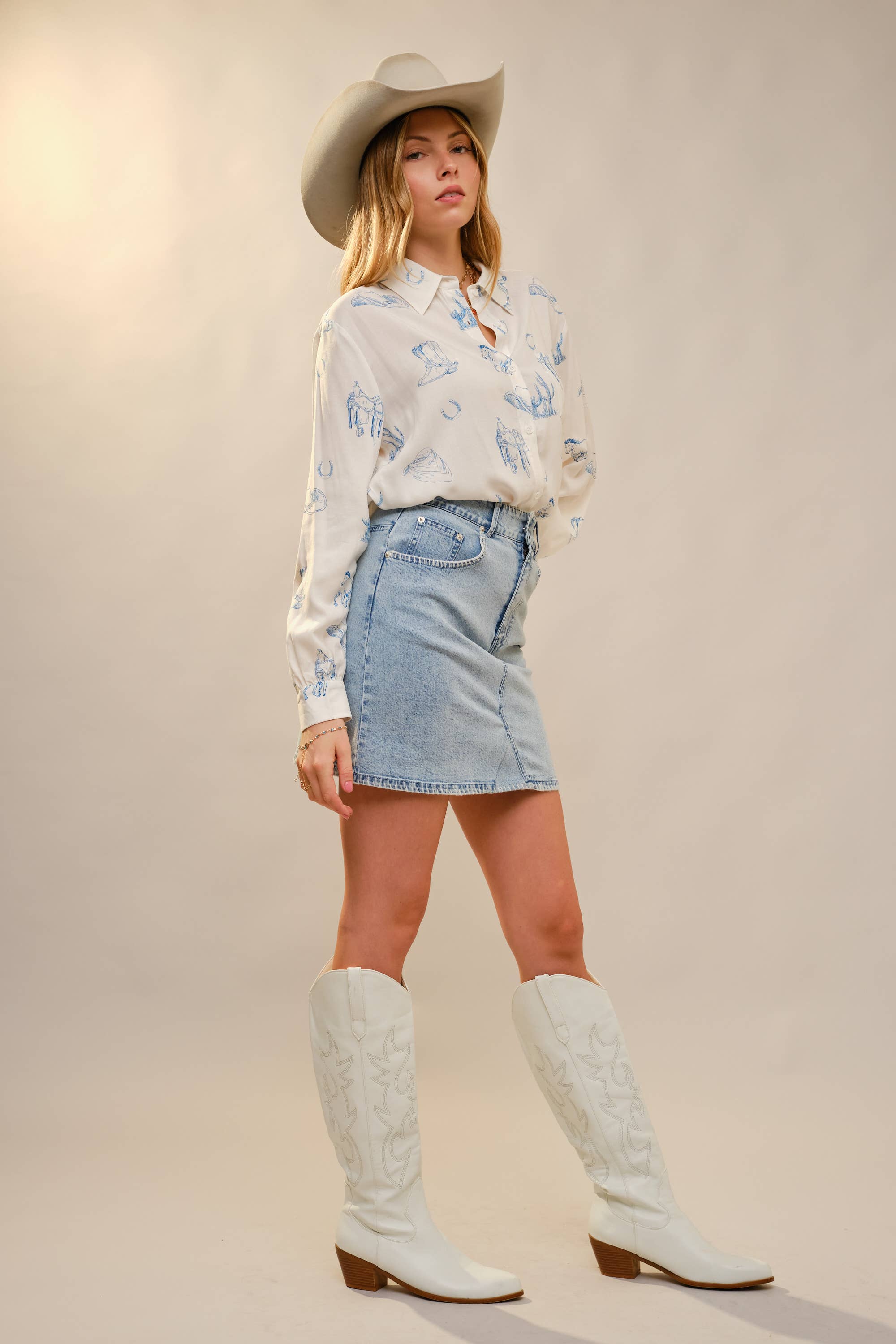 Woman wearing a floral blouse, denim skirt, and white cowboy boots on a plain background