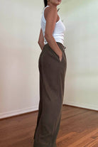 Person wearing brown high-waisted  corduroy wide leg pants and a white top in a room with a wooden floor.