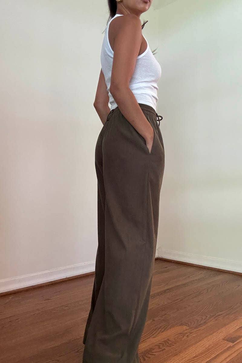 Person wearing brown high-waisted  corduroy wide leg pants and a white top in a room with a wooden floor.