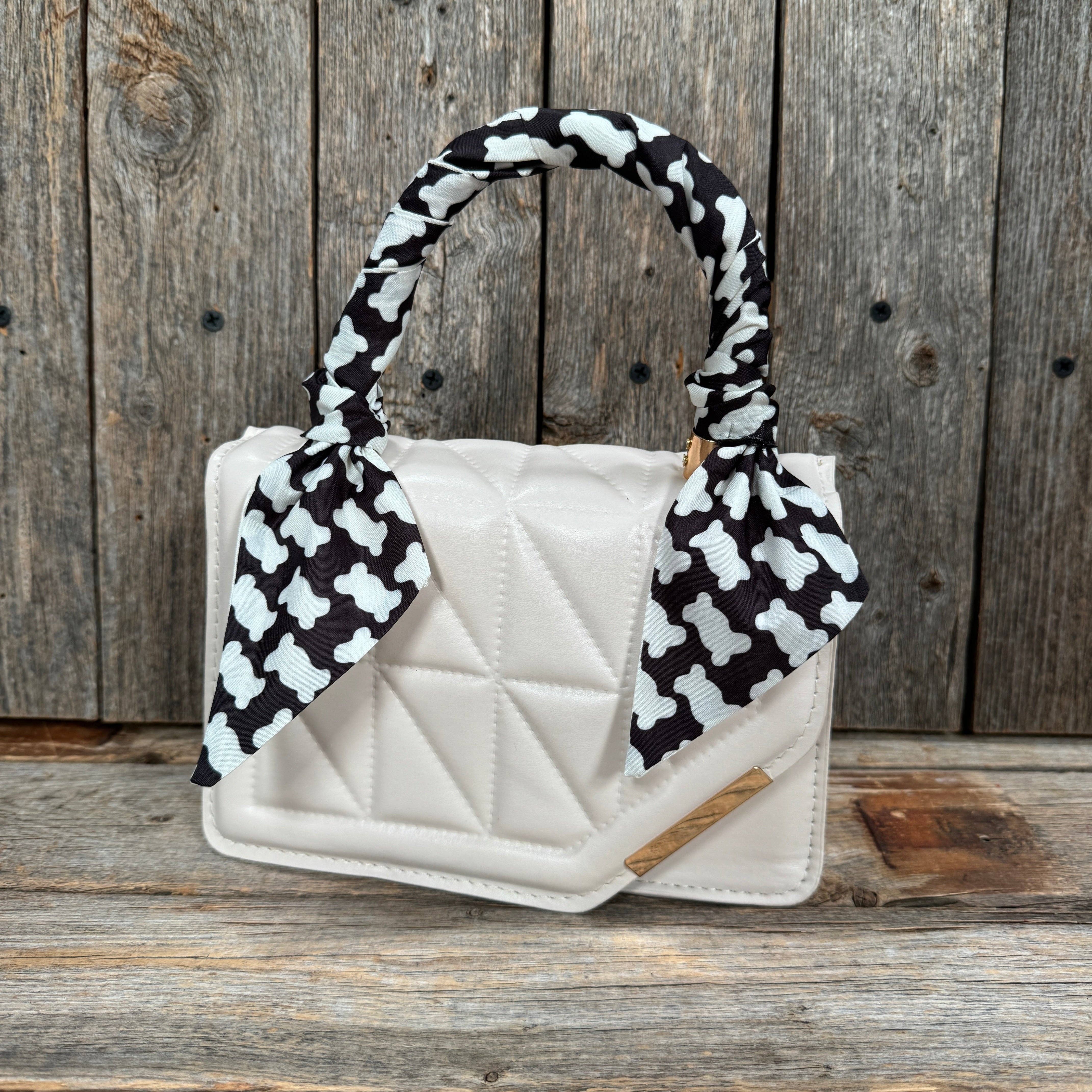 White quilted handbag with black and white patterned handle against a wooden background