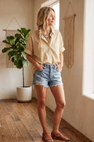 Woman standing in a room with wooden floor and plant, wearing a striped shirt and denim shorts.