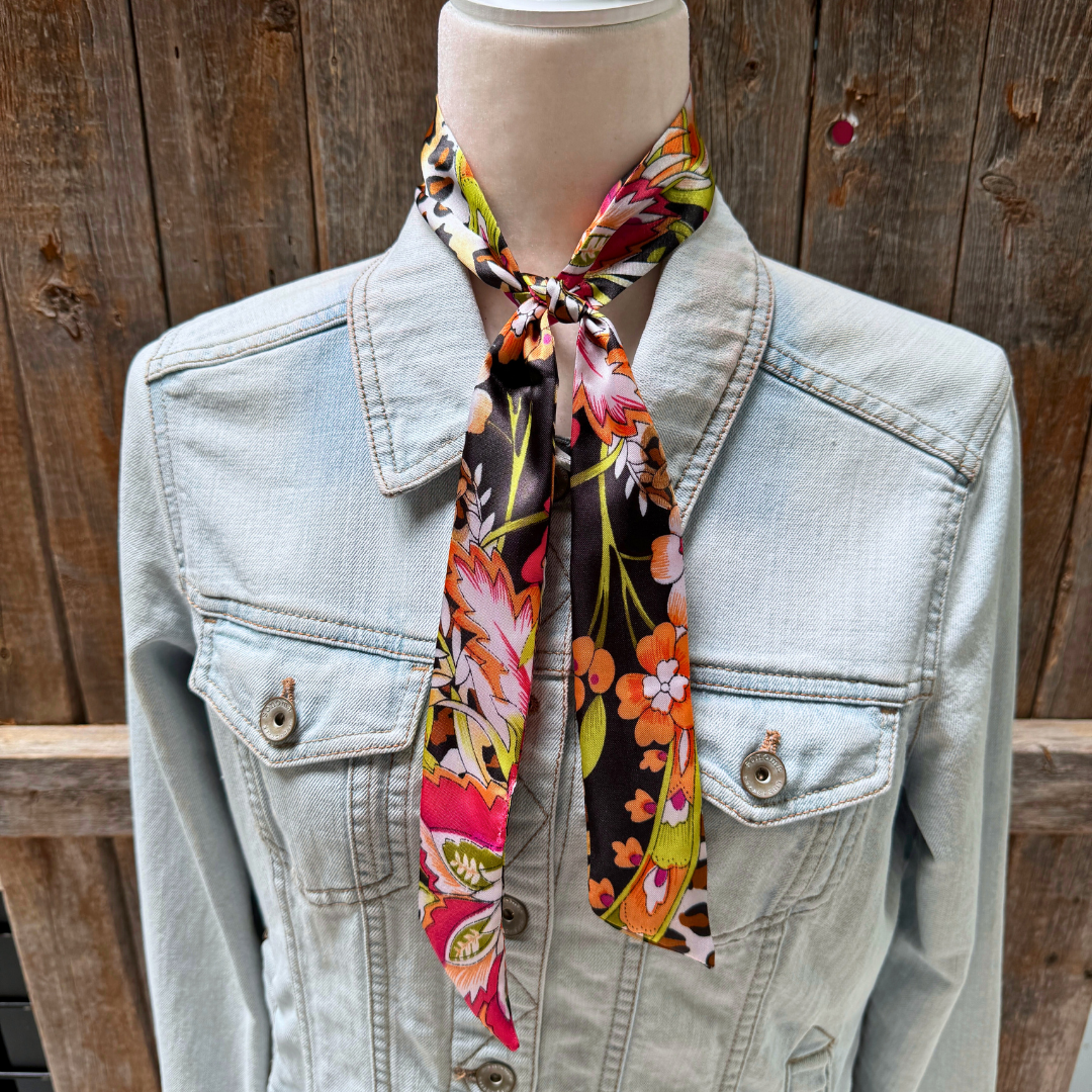 Mannequin wearing a light blue denim jacket with a colorful floral scarf draped over the neck against a wooden background.