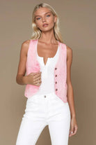 Woman wearing a pink vest over a white top and pants on a beige background