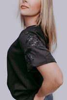Person wearing a black t-shirt with sequin horse details on a plain background