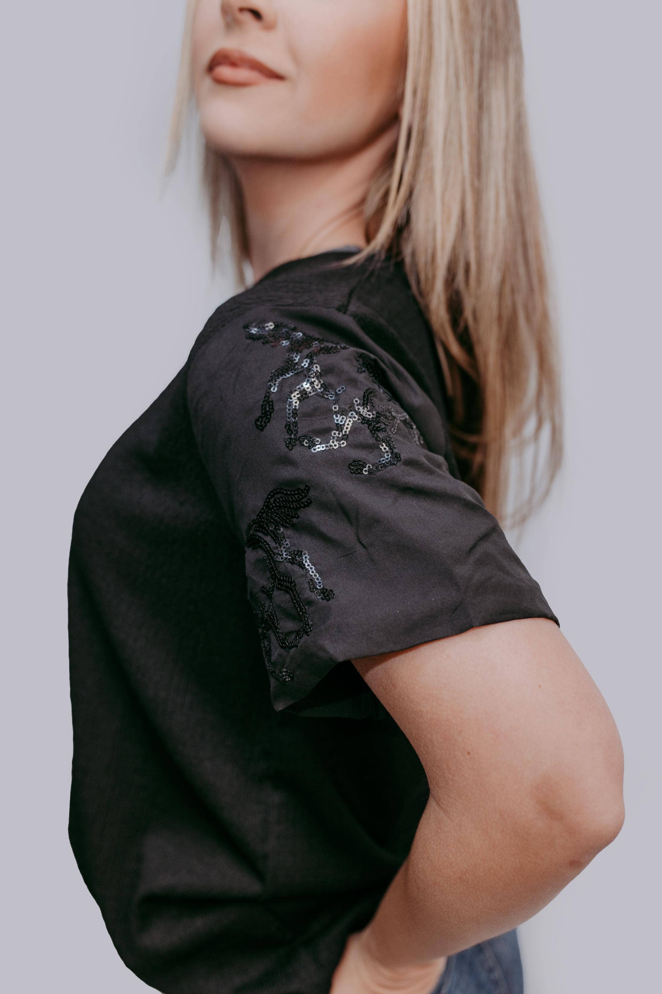 Person wearing a black t-shirt with sequin horse details on a plain background