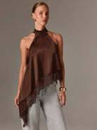 Woman wearing a brown halter top with lace details on a plain background