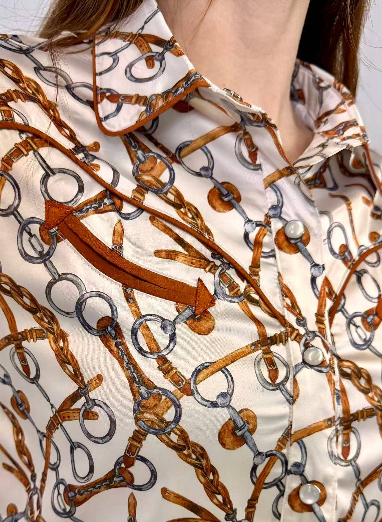 Close-up of a shirt with a pattern of brown horsewhips and silver rings on a white background.