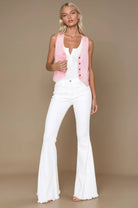 Woman wearing a pink vest over a white top and flared pants on a beige background