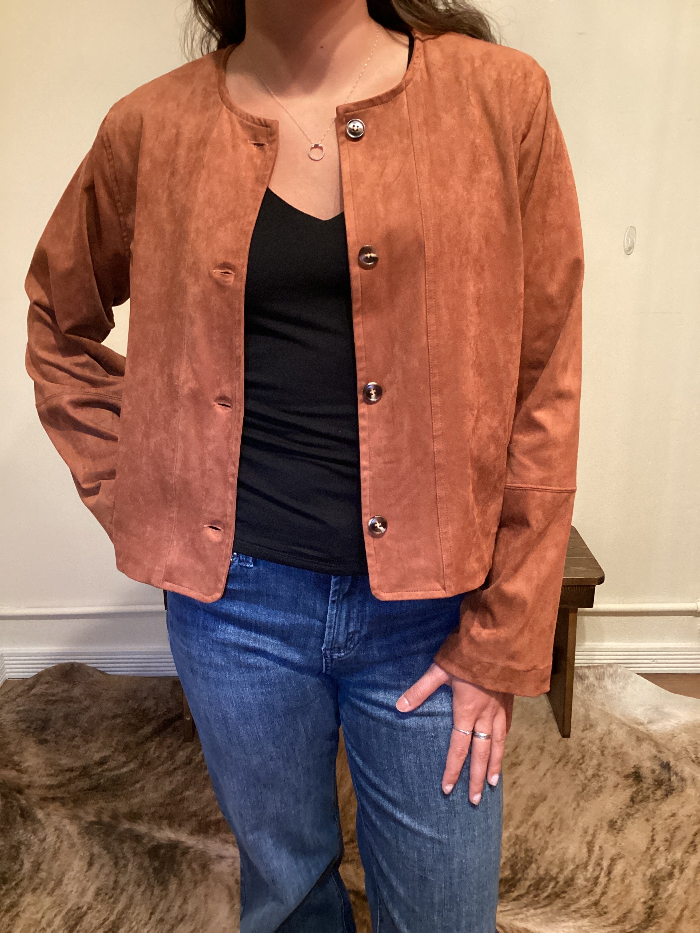 Person wearing a brown faux leather button up jacket and blue jeans 