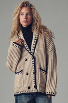 Woman wearing a beige knitted cardigan with black buttons on a gray background