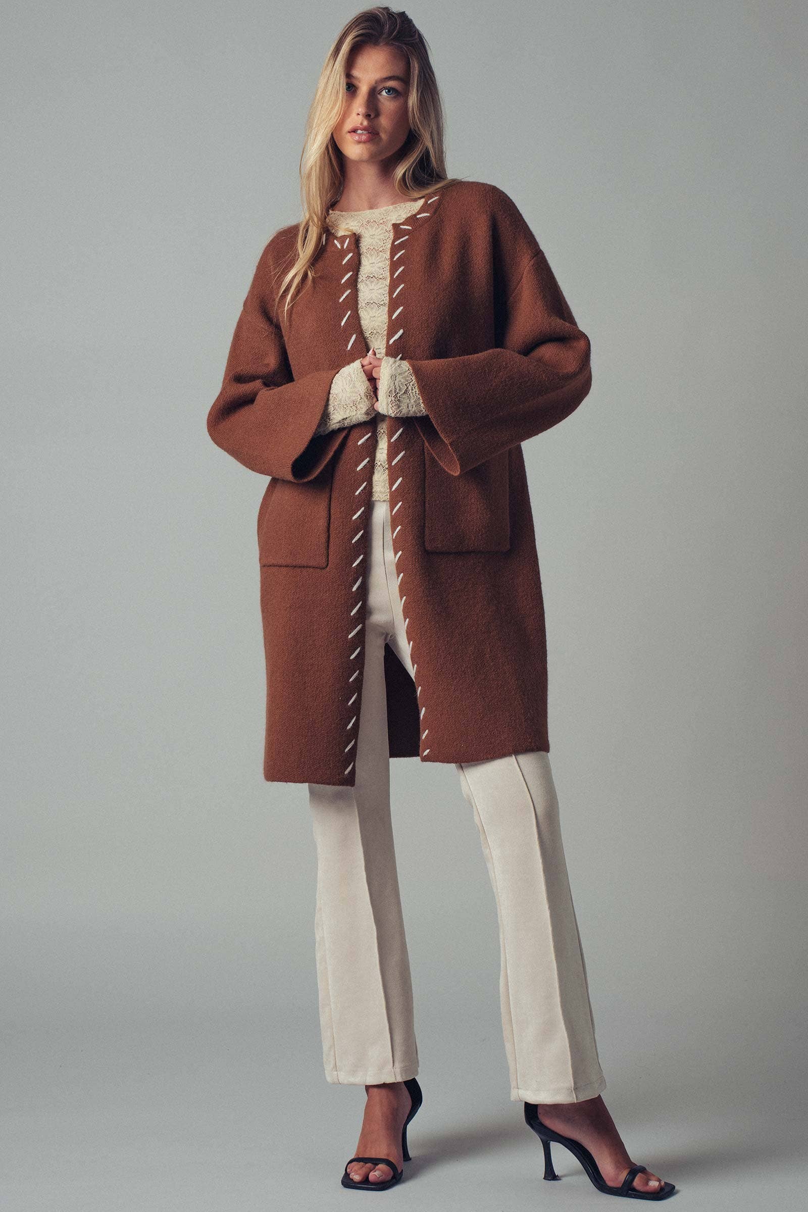 Woman wearing a brown open coat with white bold stitching  trim 