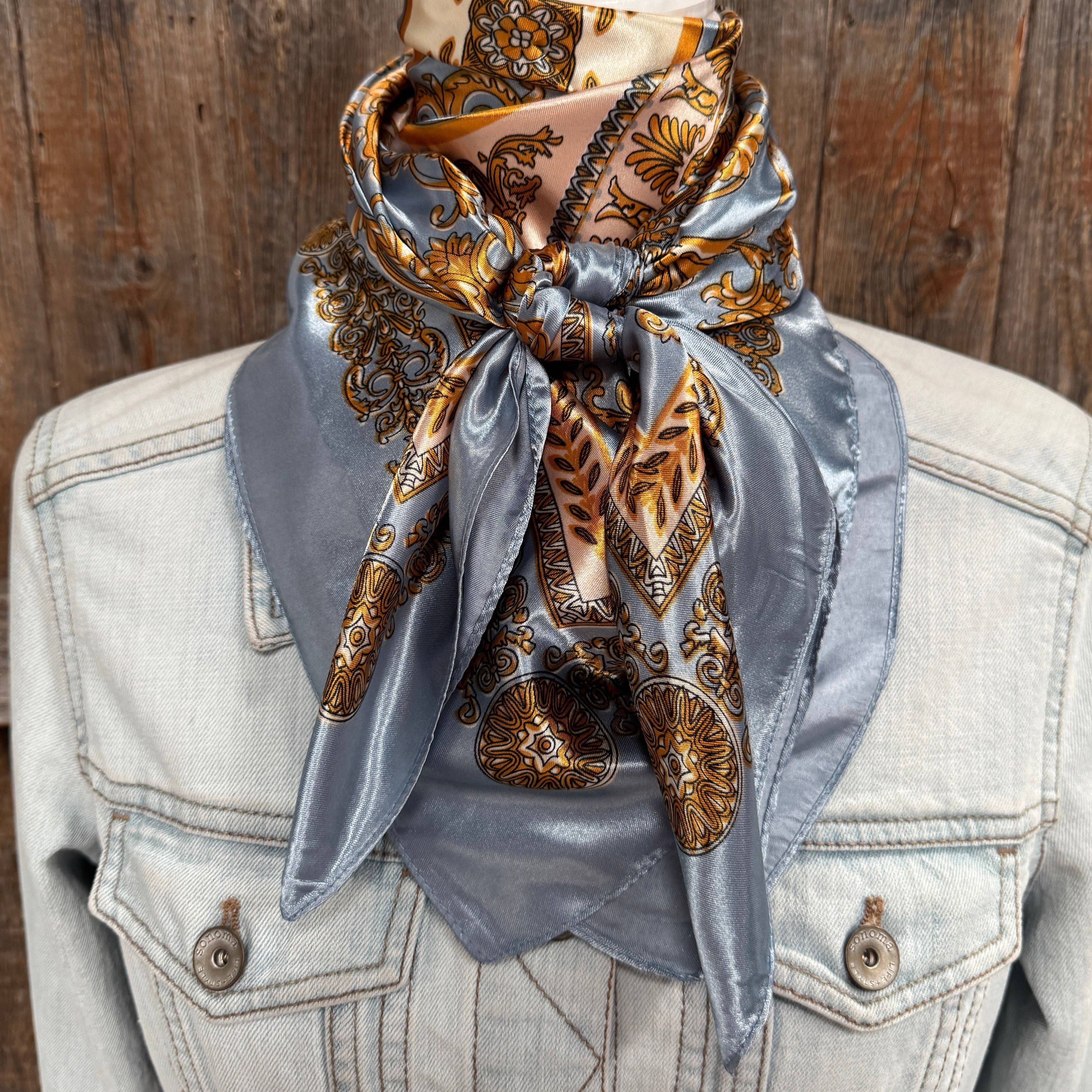 Decorative scarf with gold and brown patterns on a light blue fabric draped over a denim jacket against a wooden background.