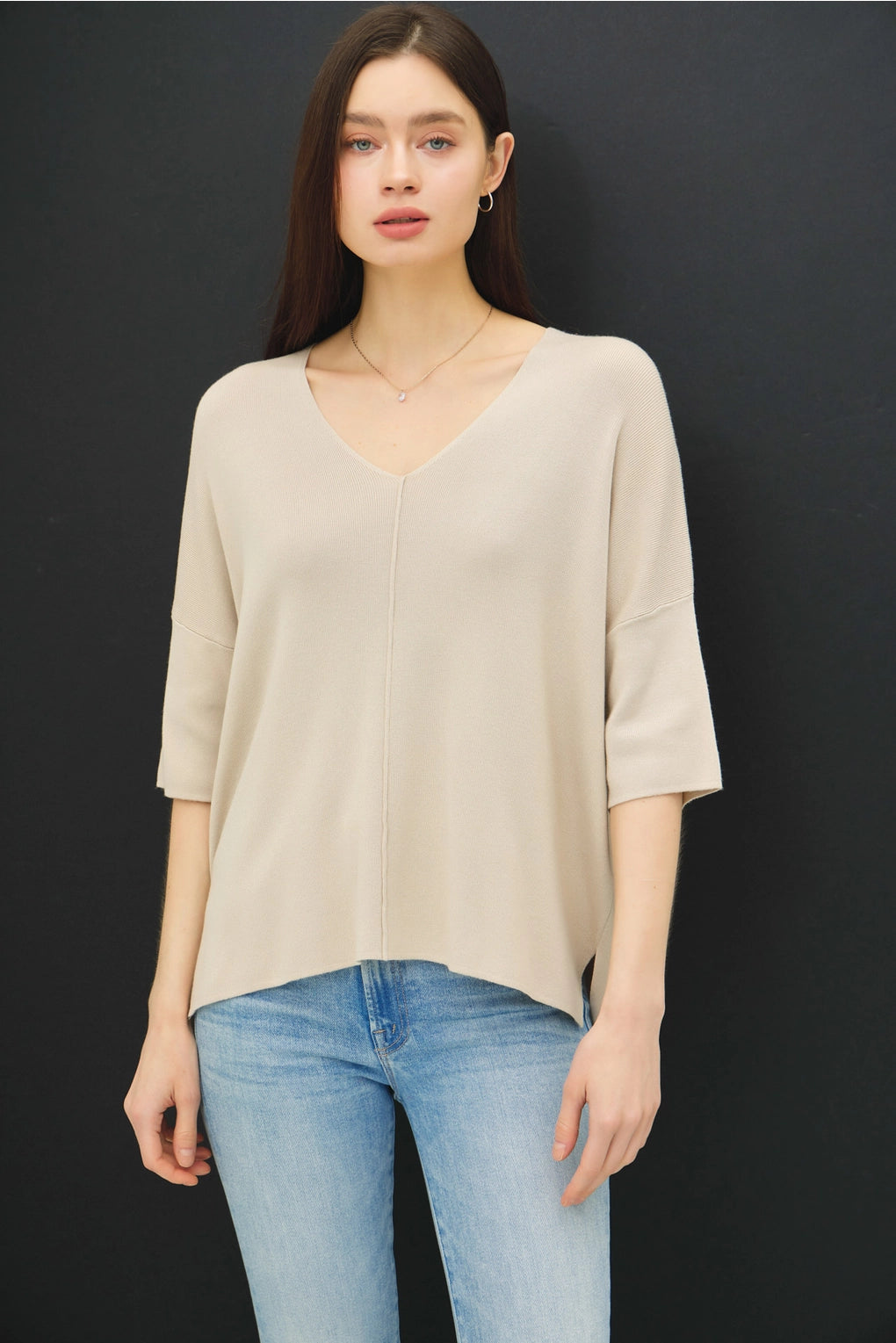 Woman wearing a beige top and blue jeans against a black background