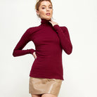 Woman wearing a burgundy turtleneck sweater and beige skirt on a white background