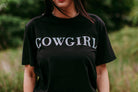 Person wearing a black t-shirt with 'COWGIRL' text in a field