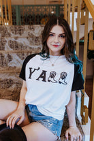Woman wearing a white t-shirt with 'Y'ALL' printed on it, sitting on a staircase.