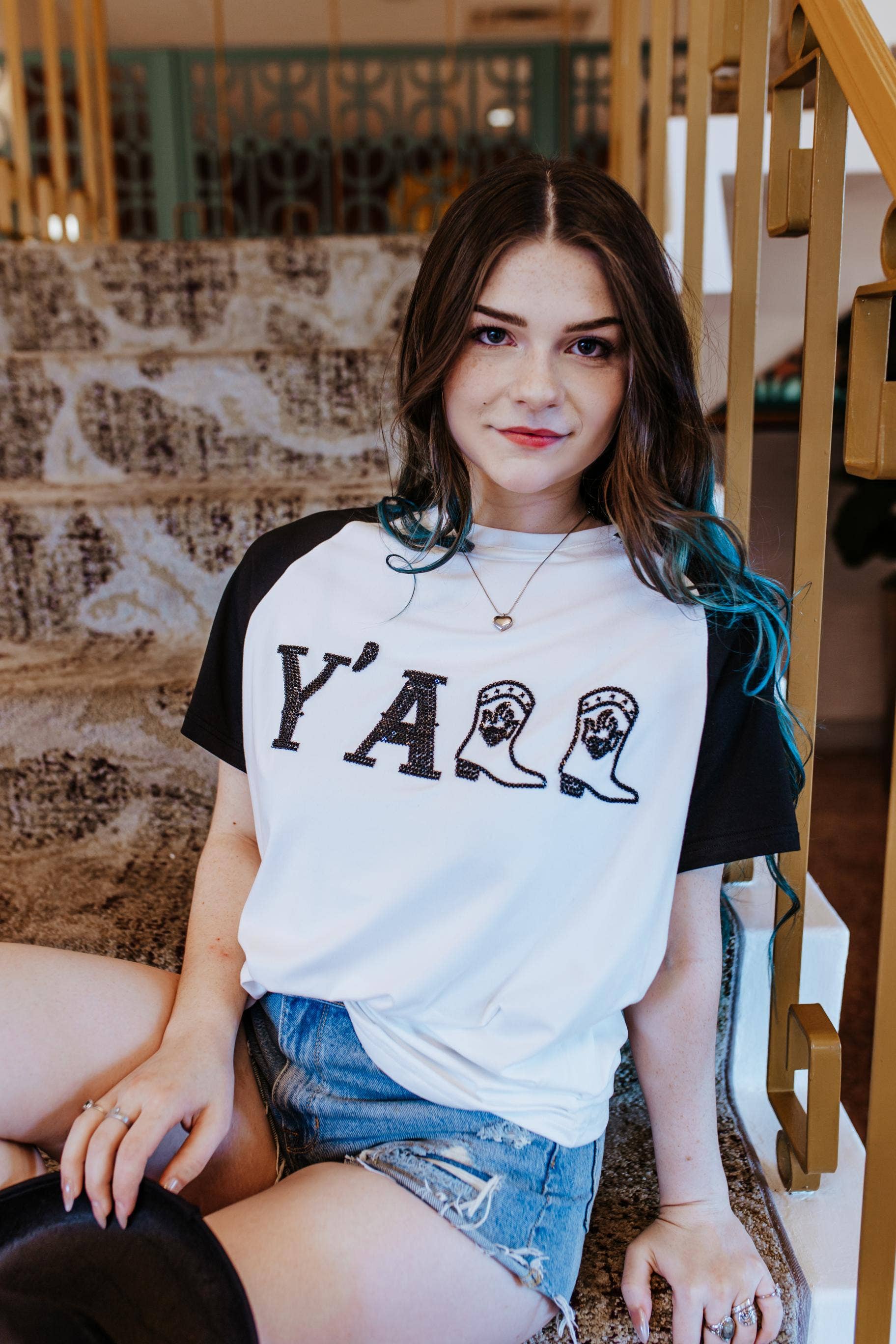 Woman wearing a white t-shirt with 'Y'ALL' printed on it, sitting on a staircase.