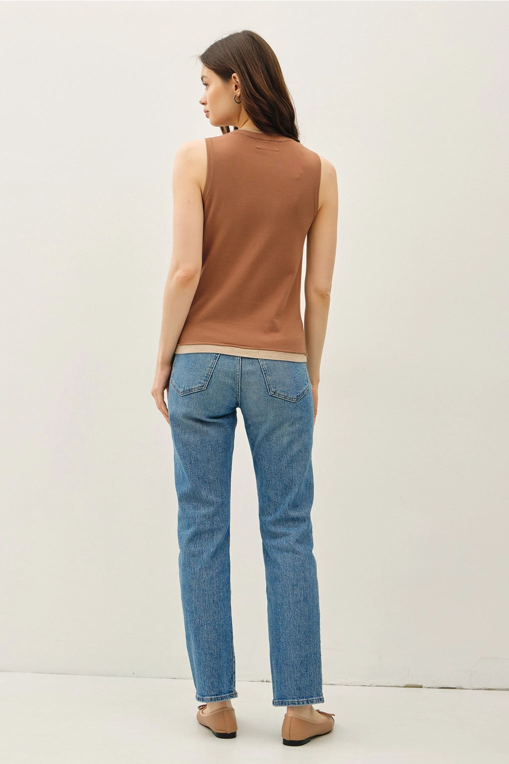 Woman wearing a brown sleeveless top and blue jeans on a white background