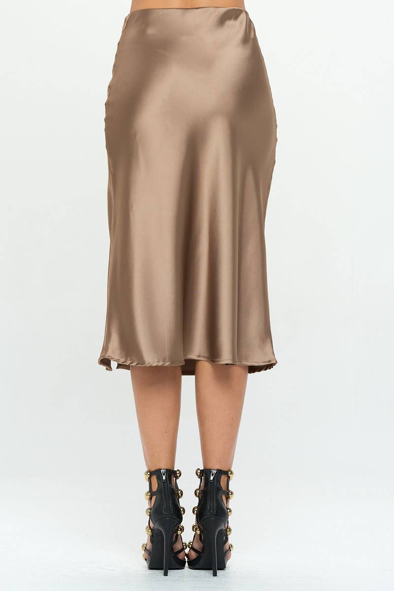 A woman modeling a satin midi skirt with a side slit, in a metallic color, paired with a satin top with a bow detail.