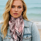 Woman wearing a pink and gray patterned scarf with a denim jacket on a beach.