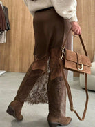 Person wearing brown lace pants and boots, holding a matching brown handbag.