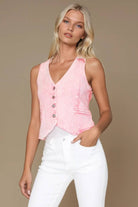 Woman wearing a pink sleeveless top and white pants against a beige background