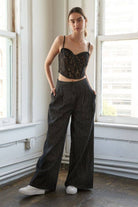 Woman wearing a black lace cropped top and wide-leg pants in a room with large windows.
