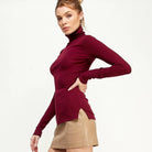 Woman wearing a burgundy long-sleeve top and beige skirt on a white background