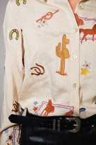 Close-up of a person wearing a cream-colored shirt with embroidered western designs.