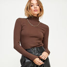 Woman wearing a brown turtleneck sweater and black leather pants on a white background