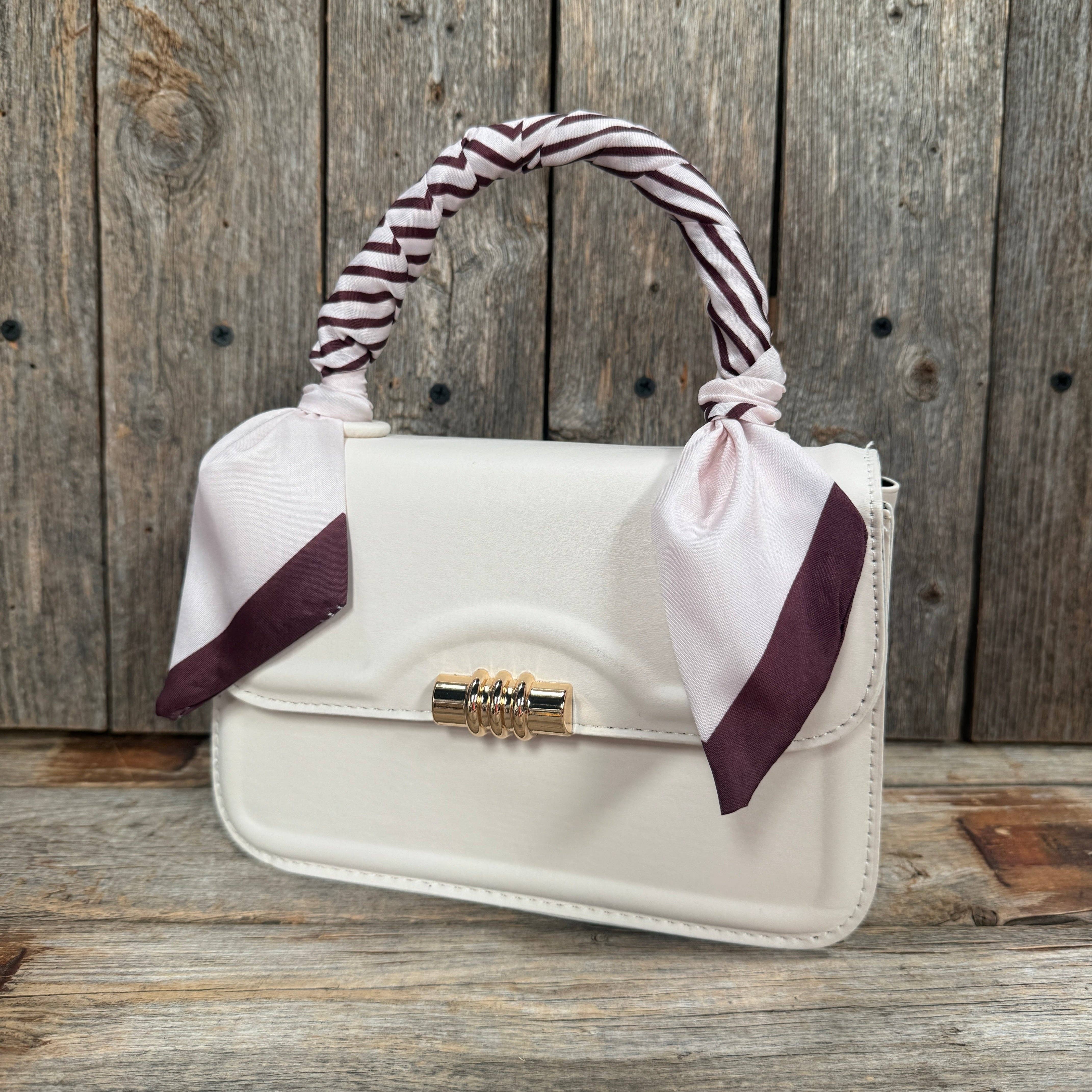 White handbag with a striped handle and ribbon on a wooden surface