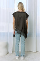 Back View: Black satin asymmetric top with lace-trim neckline, short sleeves, and diagonal lace hem, styled with light-wash jeans.